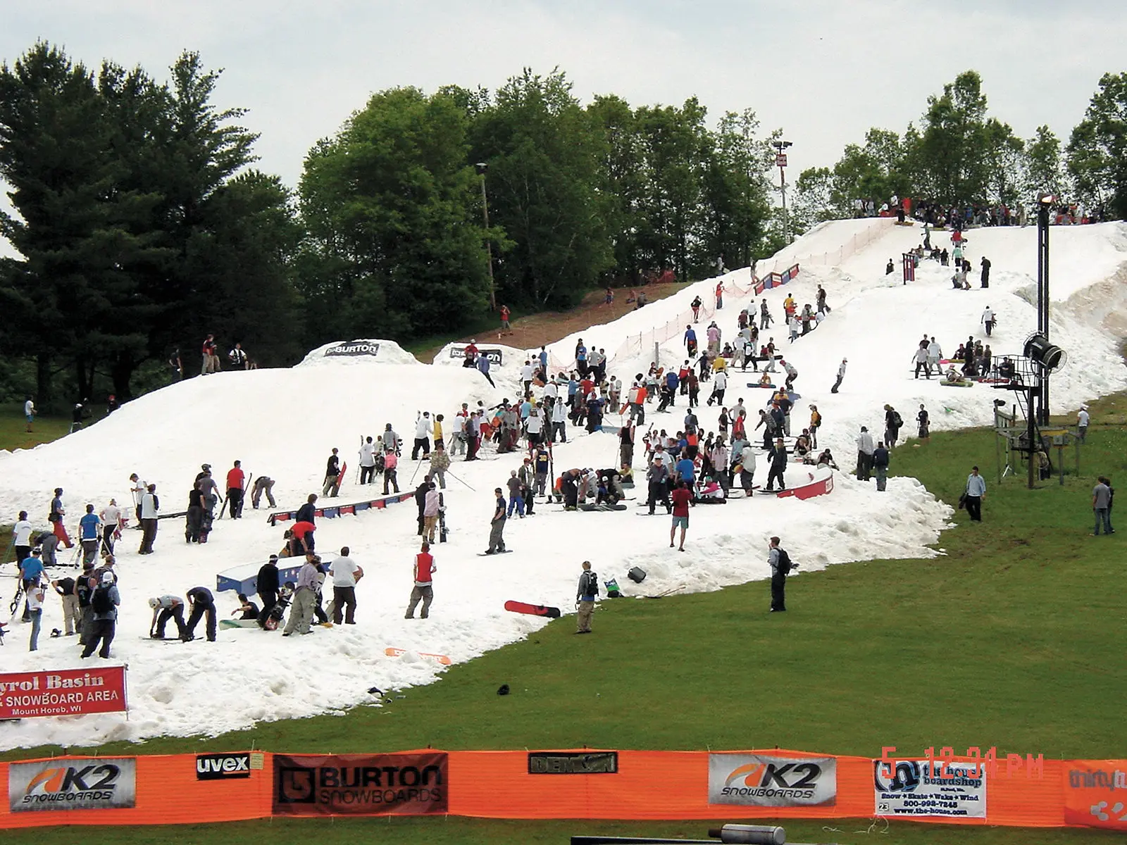 Crowd on a strip of snow on a green June hillside at Tyrol Basin