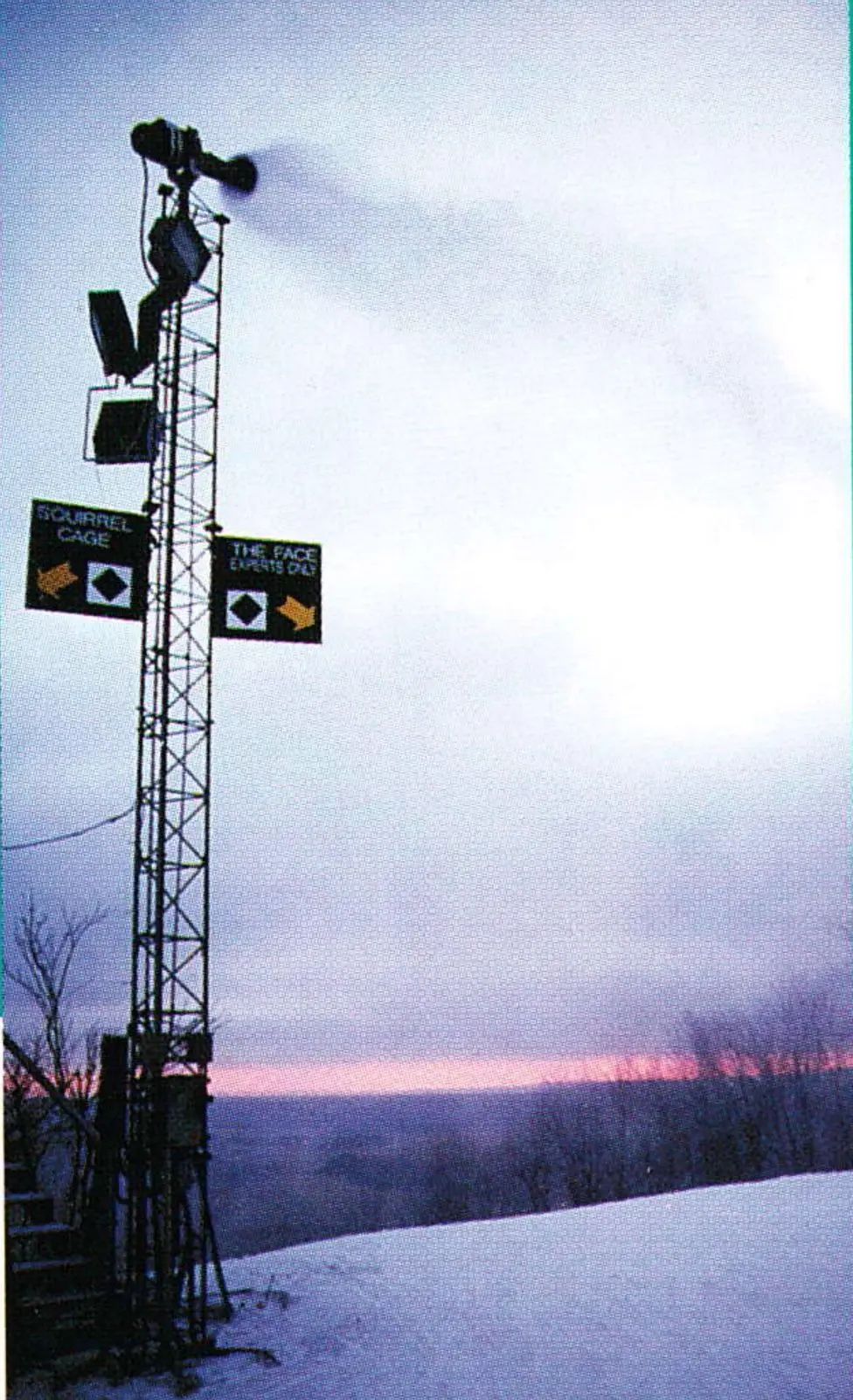 Snowmaking tower and fan gun silhouetted against a pink dusk sky over a snow-covered slope at Wisp