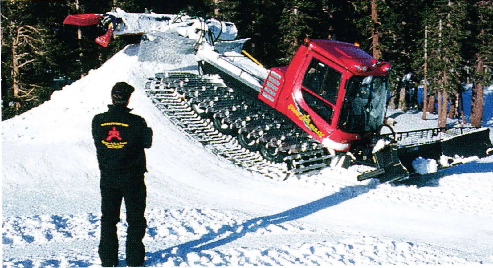 A red Pisten Bully Park Bully groomer on a snow-covered slope, with a man in a dark jacket standing in the foreground