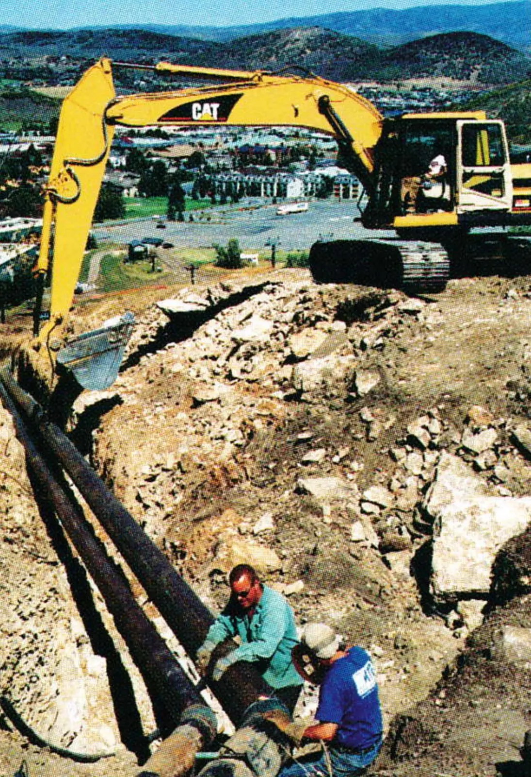 Workers laying snowmaking pipe in a trench beside an excavator at Park City