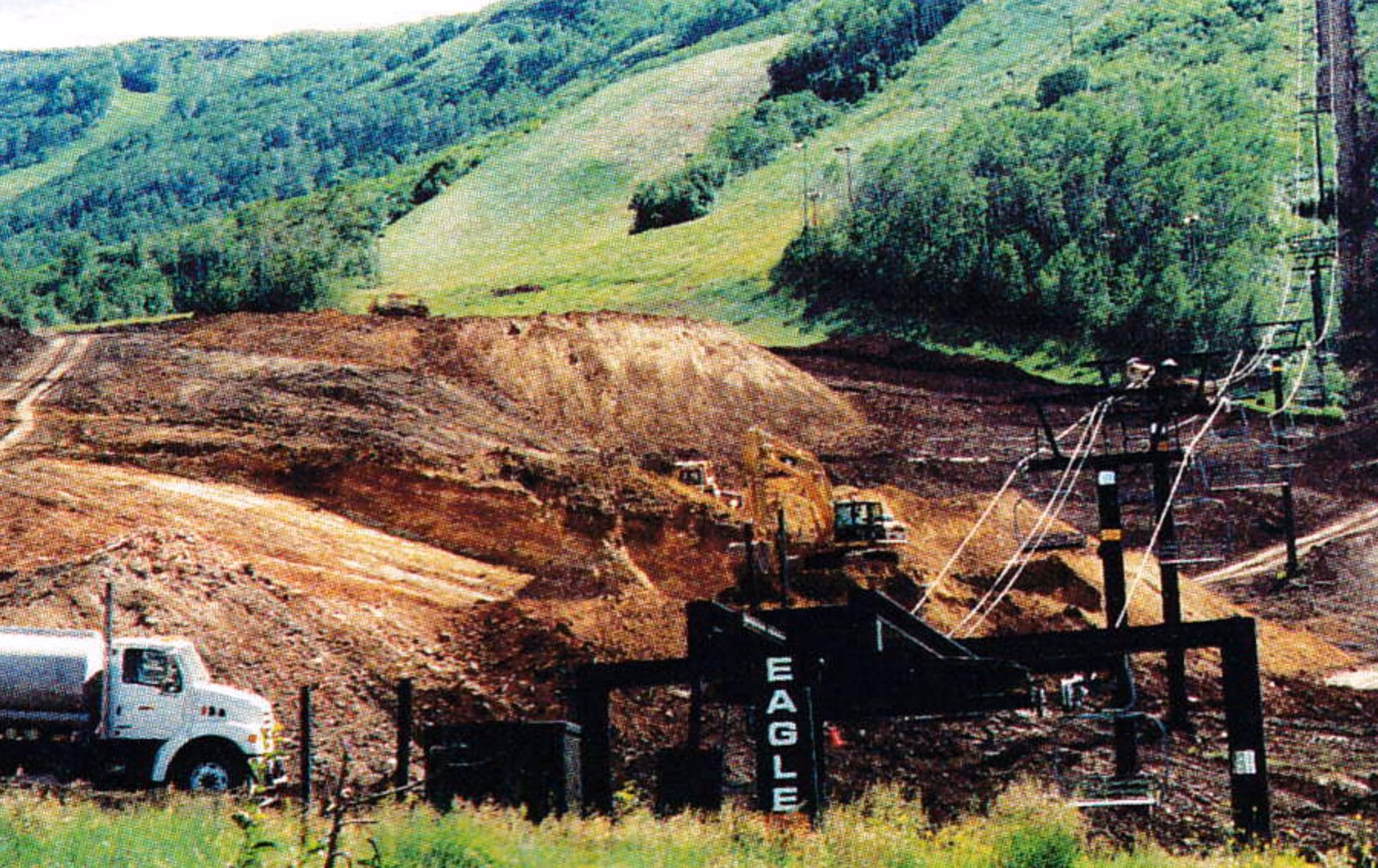 Regraded dirt slope at the bottom of the Eagle race arena, with trucks and lift towers