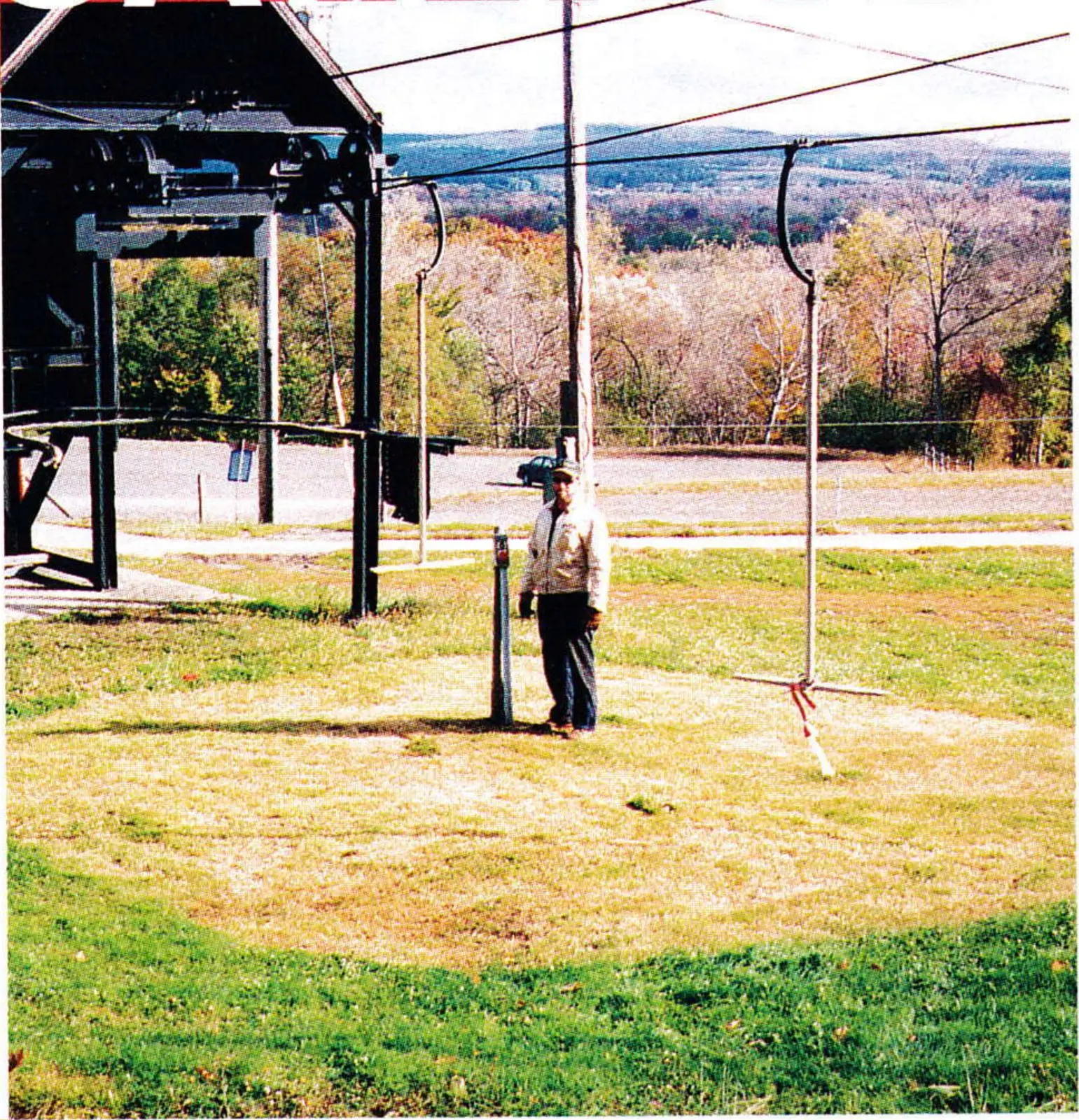 T-bar lift line over closely mowed grass at Song Mountain, with a worker standing beside a tower