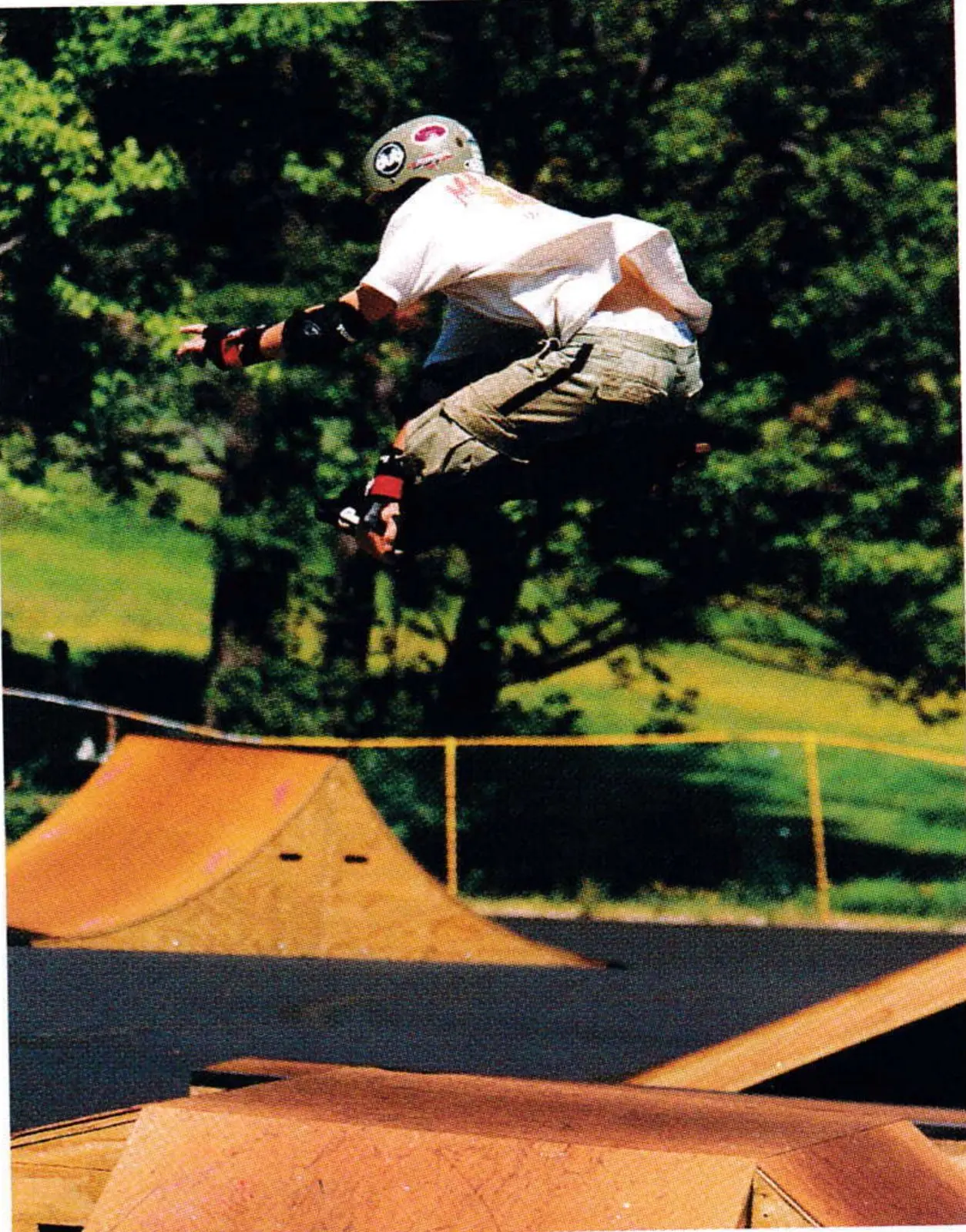 Inline skater in mid-air above wooden skatepark ramps with trees behind