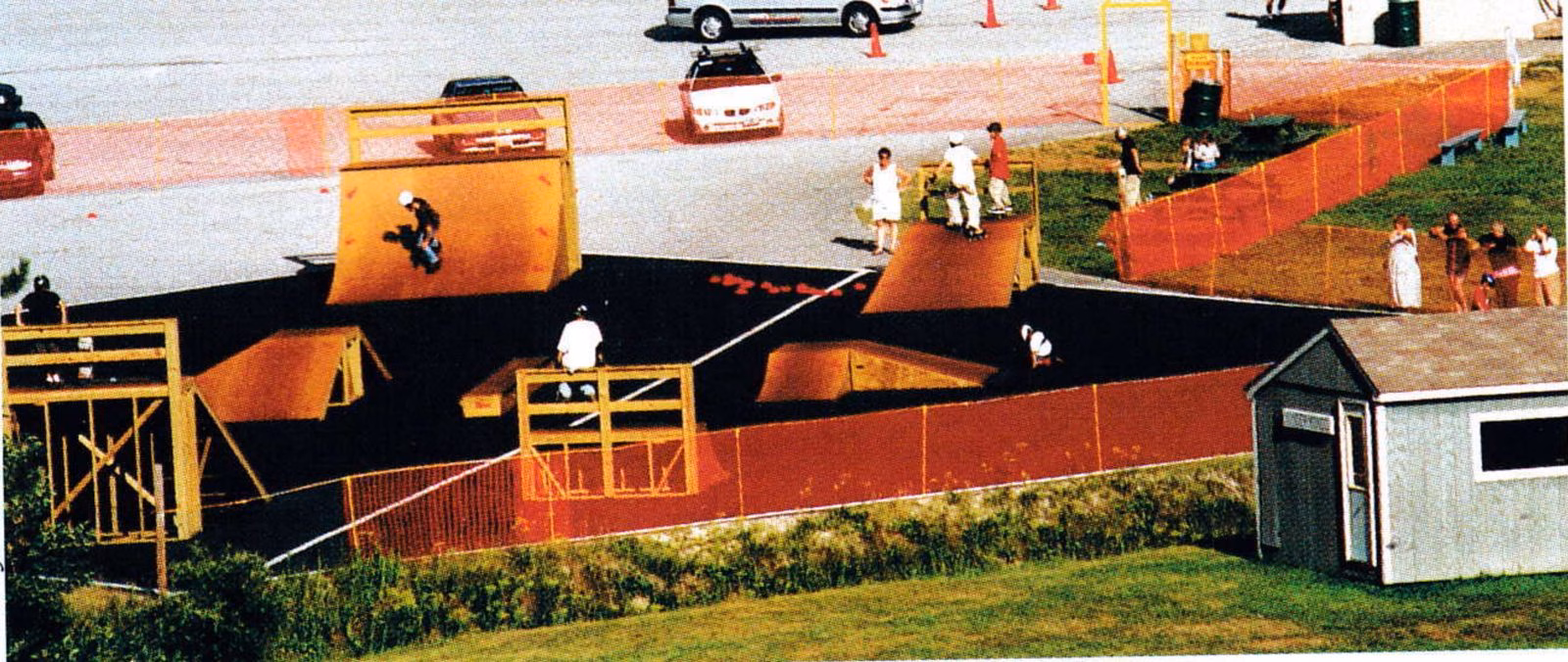 Overhead view of a fenced skatepark with wooden ramps built on a parking lot