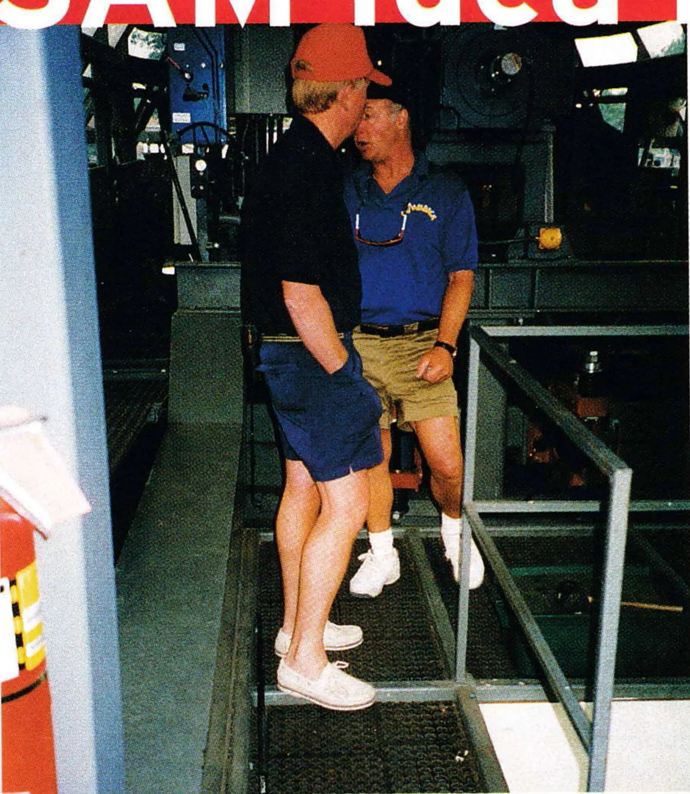 Two men standing on rubber anti-fatigue mats laid over the steel floor of a ski-lift motor room