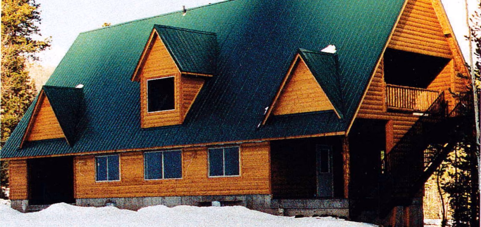 Finished log-sided ski patrol building with a green metal roof and dormers in the snow
