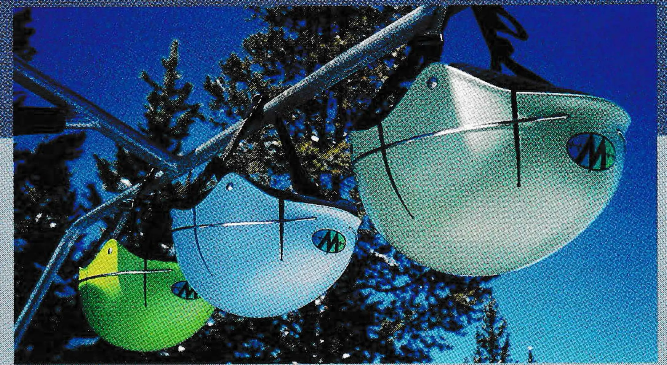 Three Team Wendy ski helmets hanging from a rack against blue sky and pine trees