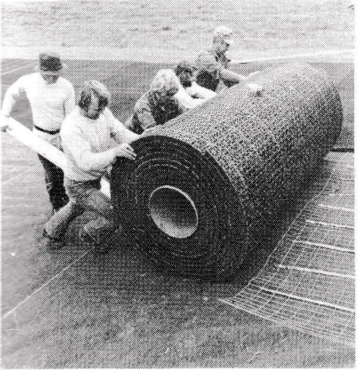 Workers push a 400-lb. roll of the Sun Slope plastic surface into place over the indoor-outdoor carpeting and wire mesh.