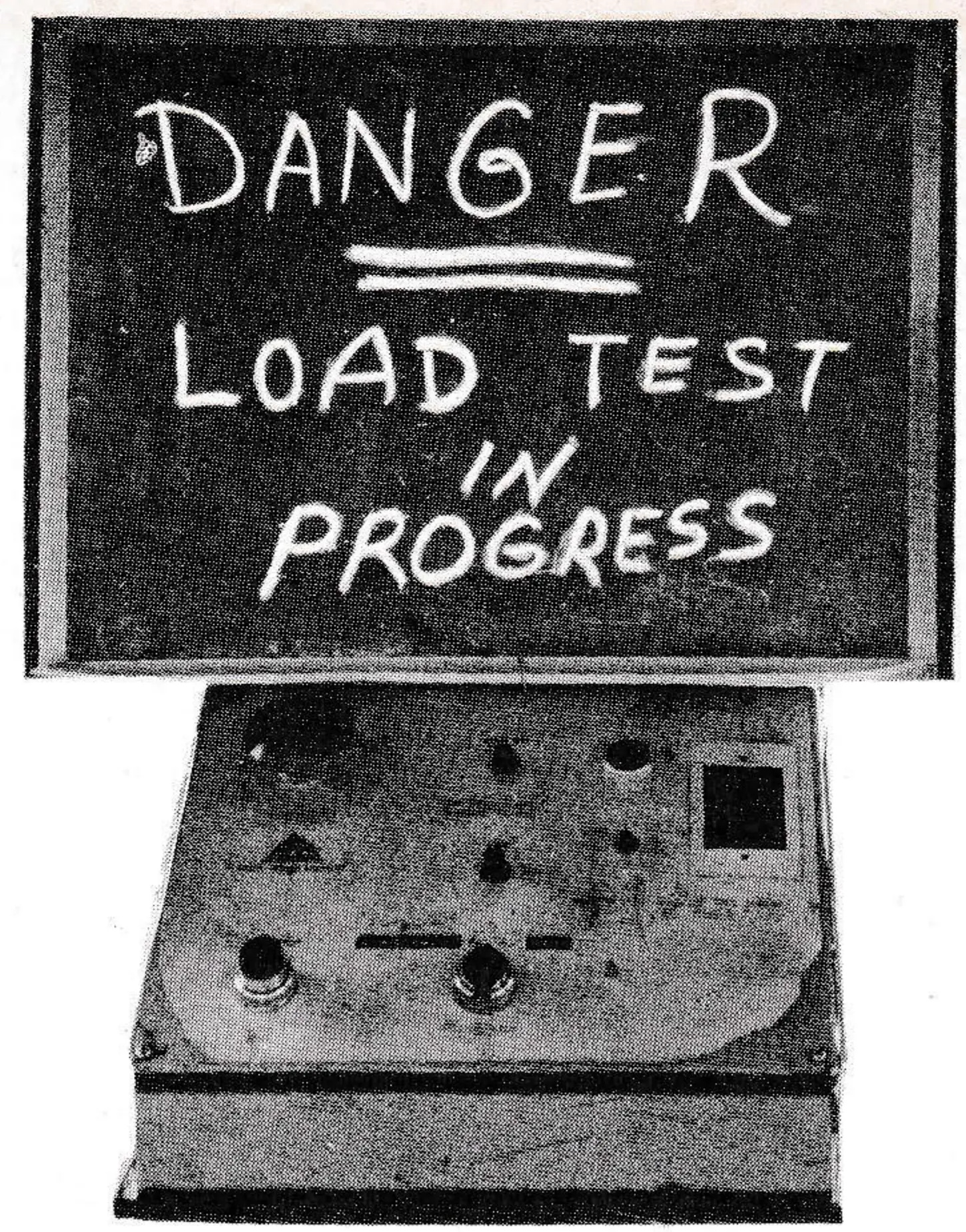 Chalkboard sign reading "Danger — Load Test in Progress" standing above an aerial lift control panel.