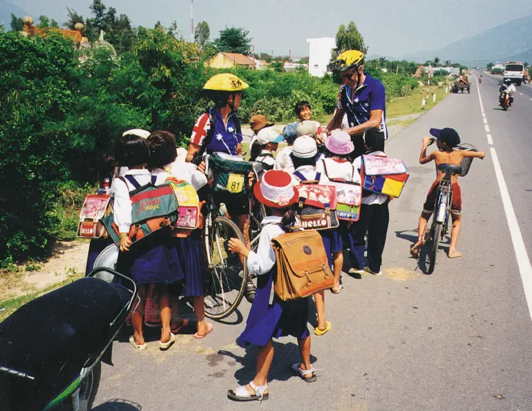 Schoolchildren crowding around touring cyclists on a roadside