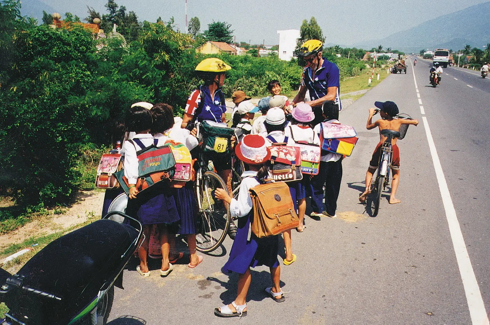Schoolchildren crowding around touring cyclists on a roadside