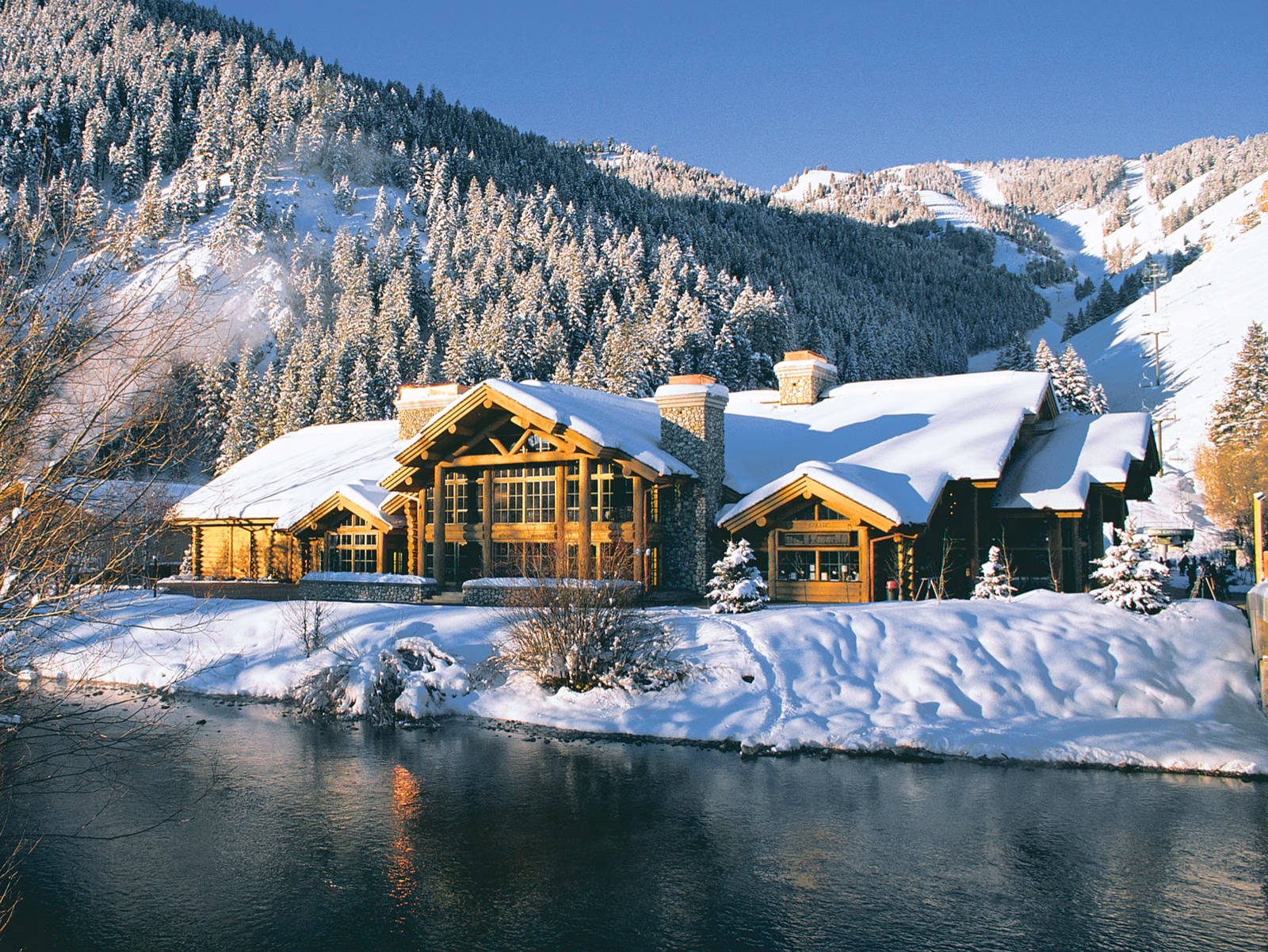 Log lodge beside a stream below snowy ski runs
